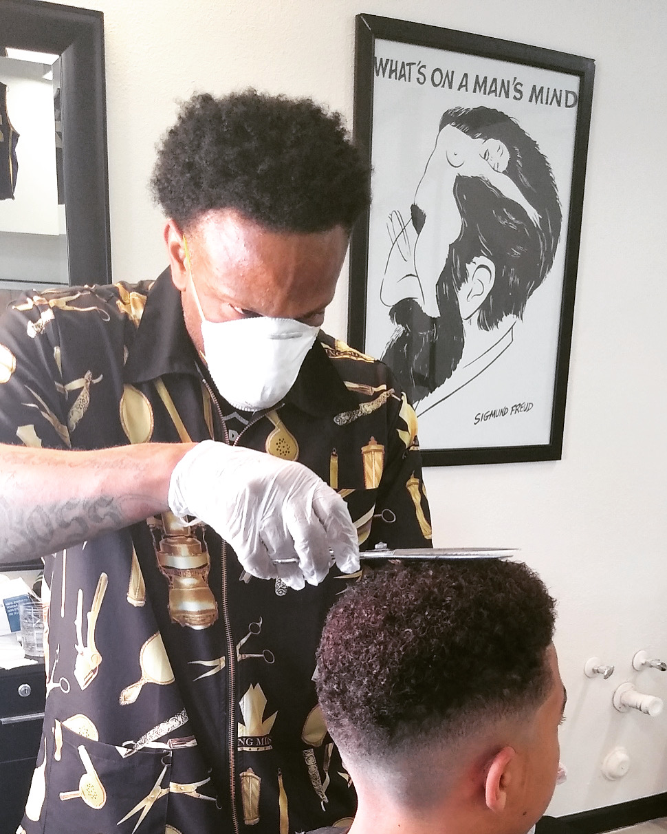 Barber in mask carefully trimming a client's fade next to a framed print