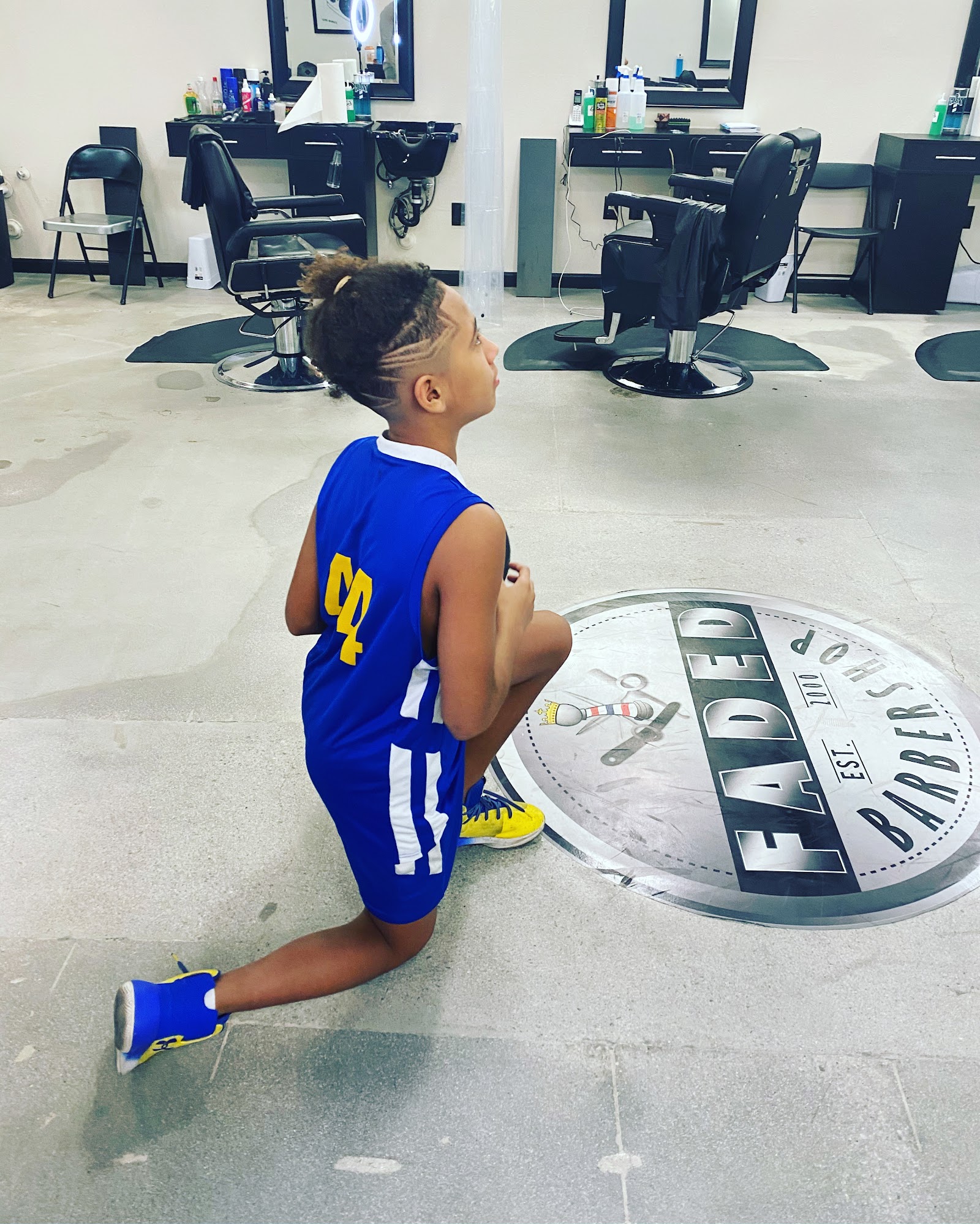 Young client with fresh haircut and hair design kneeling on the Faded Barbershop floor logo