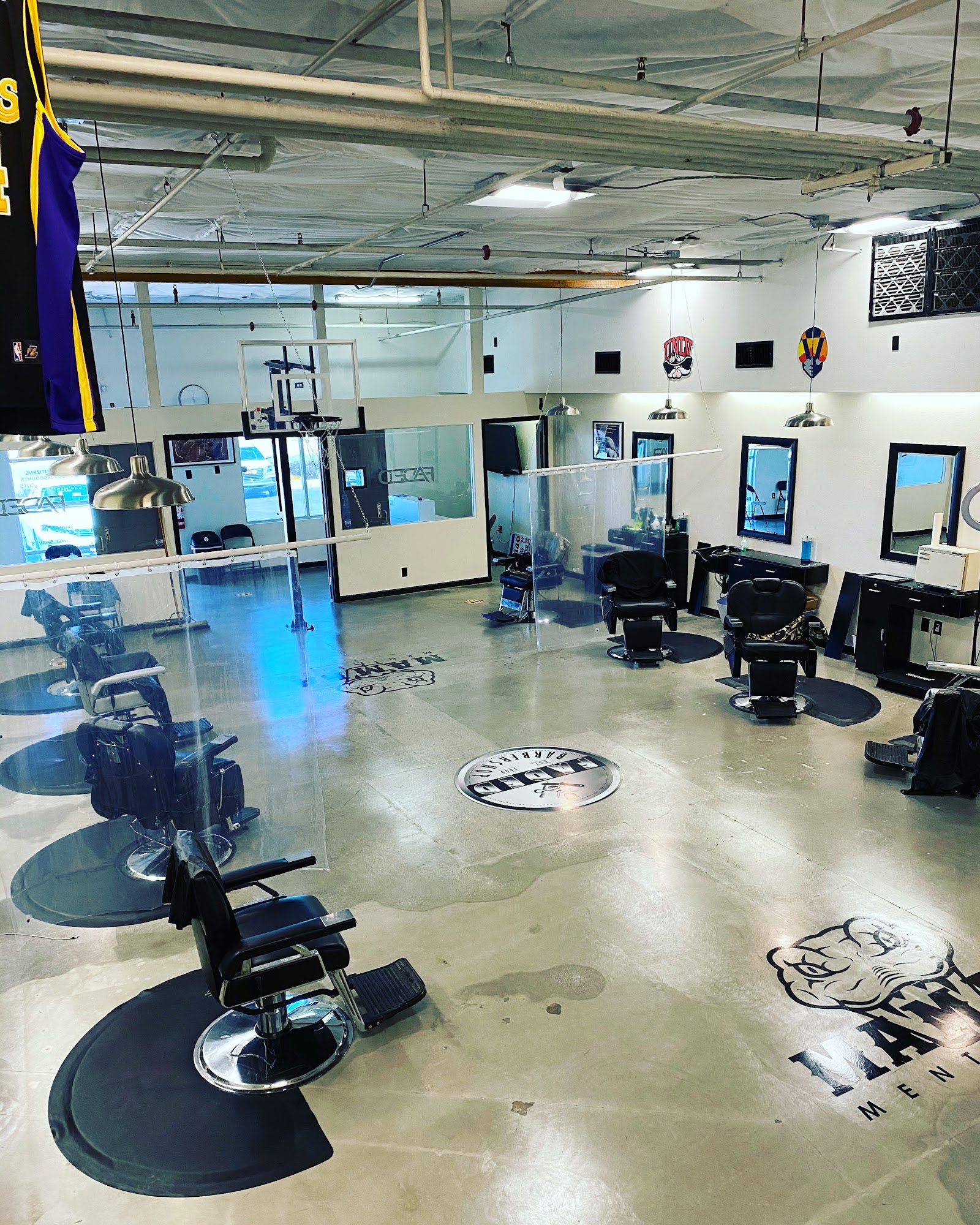 Wide interior view of Faded Barbershop with multiple barber chairs, floor logo and industrial ceiling